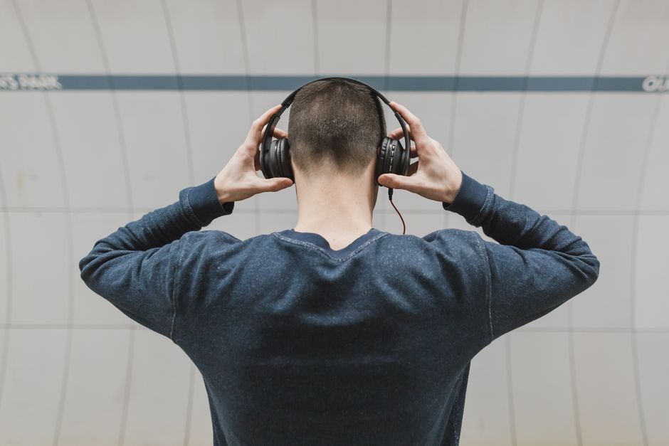 Man with headphones listening to music indoors, wearing long sleeves. Back view shot.