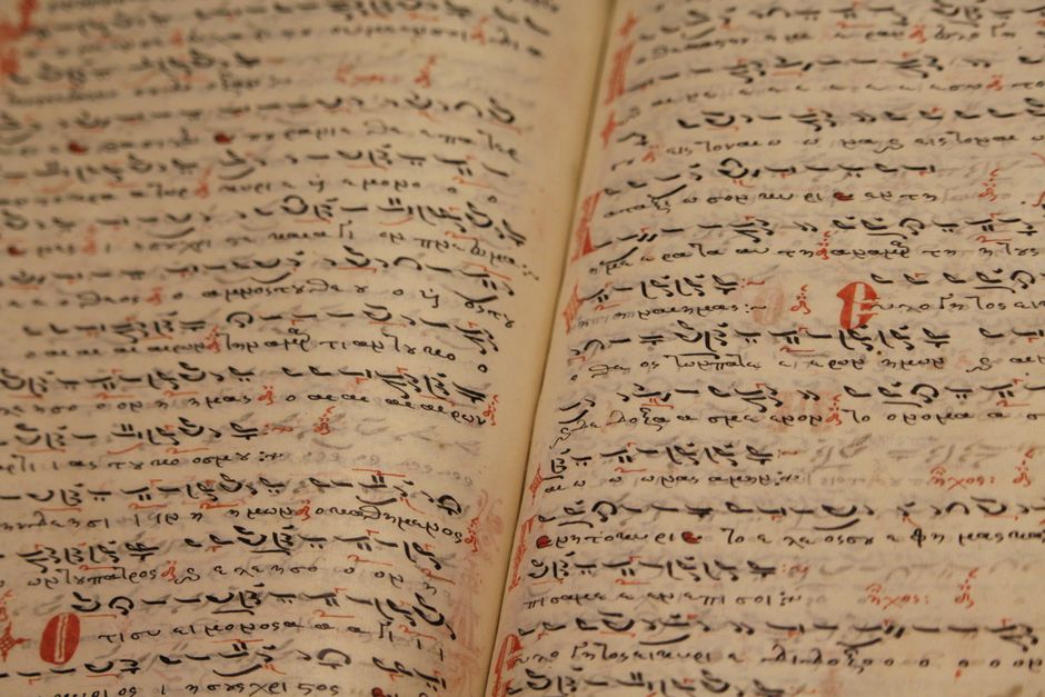 From above of ancient opened book with handwritten inscriptions in black ink in Arabic language on thin pages