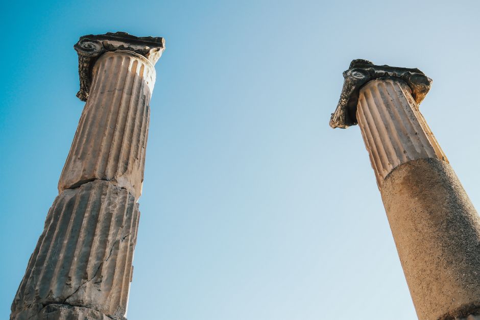 Two ancient Greek columns stand under a bright clear blue sky, showcasing historical architecture.
