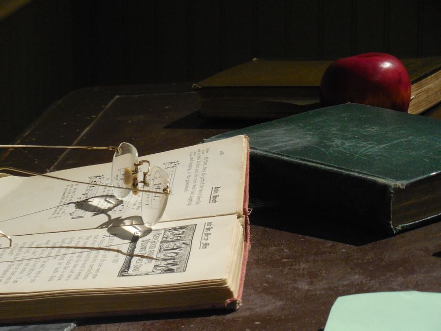 A collection of vintage books and eyeglasses on a wooden desk, creating a nostalgic ambiance.