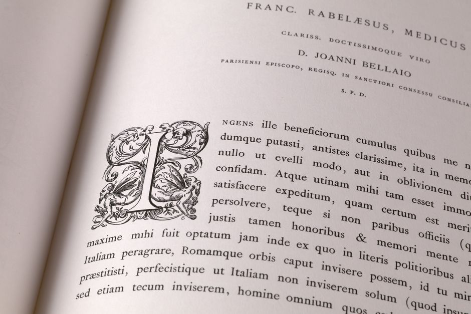 Close-up of an open book with intricate Latin text and decorative initials.