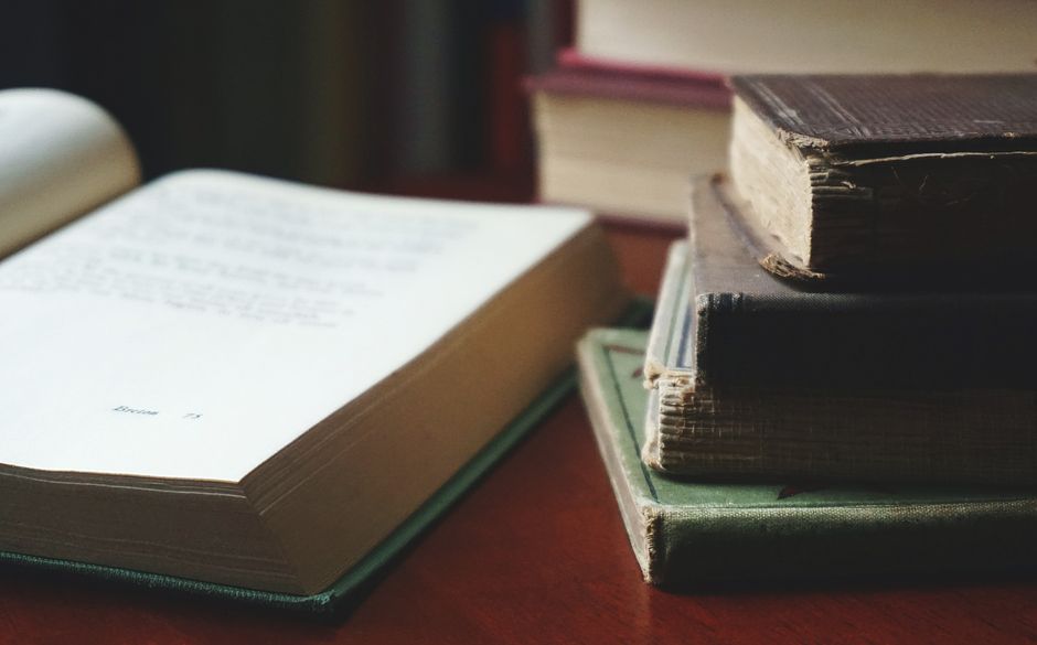 A collection of aged books stacked neatly on a wooden table for reading enthusiasts.