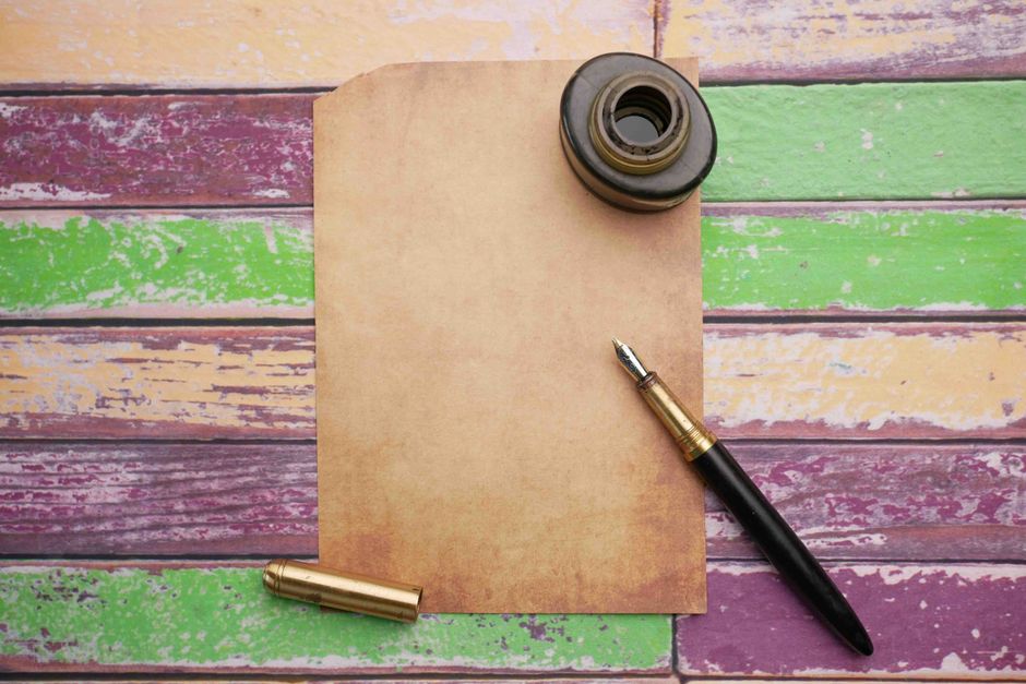 Flat lay of vintage paper with ink bottle and pen on a colorful wooden surface.