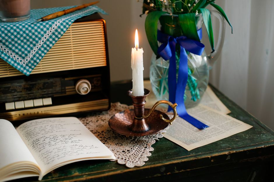 A cozy vintage still life with a candle, radio, and open notebook on a table.