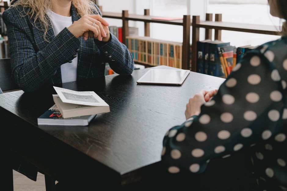 Crop anonymous females discussing literature while sitting at table with books in library cafe