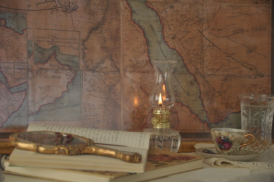An atmospheric still life featuring an oil lamp, vintage map and tea cup on a table.